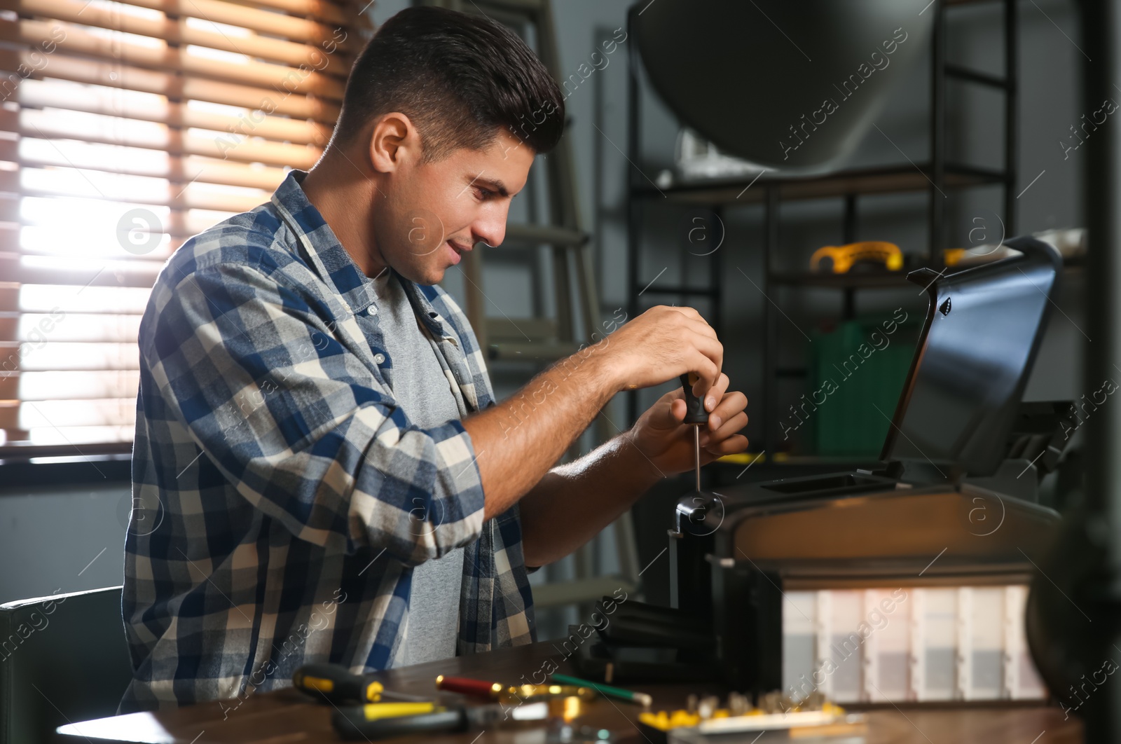 Photo of Repairman with screwdriver fixing modern printer in office