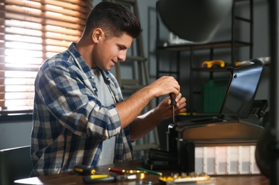 Photo of Repairman with screwdriver fixing modern printer in office