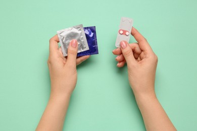 Photo of Woman with condoms and contraceptive pills on turquoise background, top view. Choosing birth control method