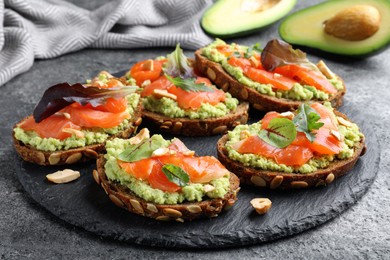 Photo of Delicious sandwiches with salmon, avocado and herbs on grey table, closeup