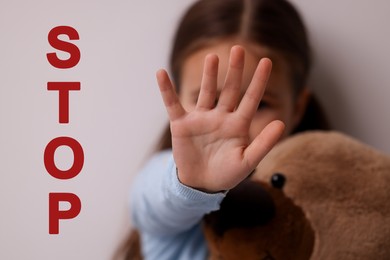 Image of No child abuse. Little girl making stop gesture on light background, selective focus