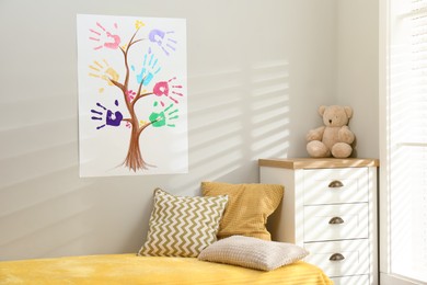 Painting with family tree of colorful palm prints on light wall over bed in child's room