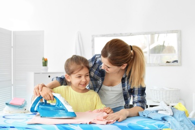 Photo of Housewife with daughter ironing clothes in laundry room