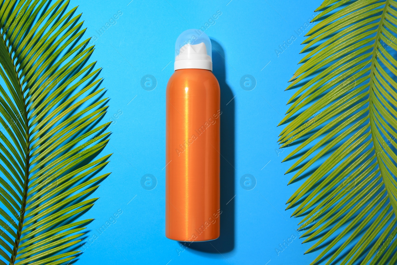 Photo of Sunscreen and tropical leaves on light blue background, flat lay. Sun protection care