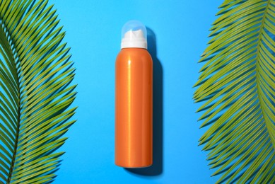 Photo of Sunscreen and tropical leaves on light blue background, flat lay. Sun protection care