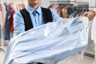 Photo of Dry-cleaning service. Woman holding shirt in plastic bag indoors, closeup