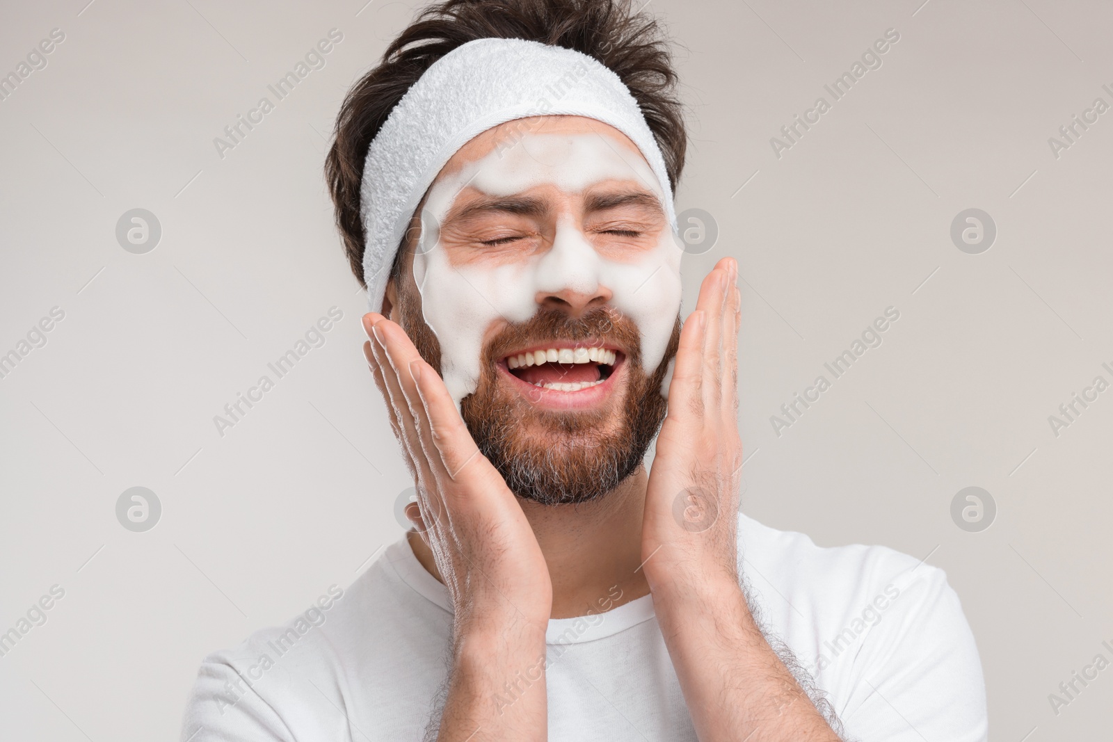 Photo of Man with headband washing his face on light grey background