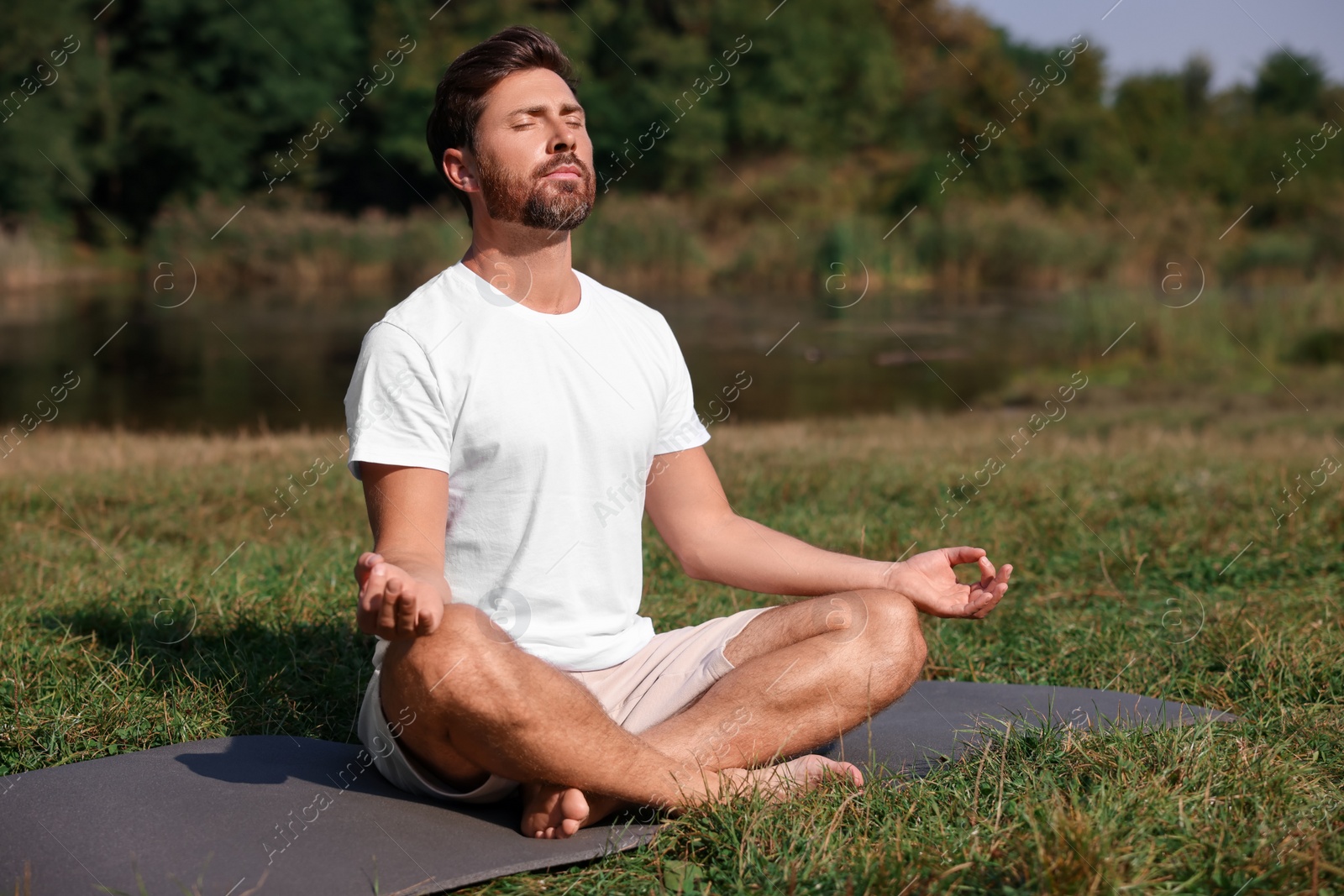 Photo of Man practicing yoga on mat outdoors. Lotus pose