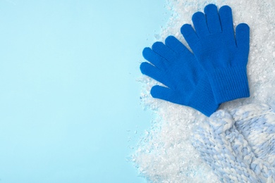 Photo of Stylish woolen gloves, hat and artificial snow on light blue background, flat lay. Space for text