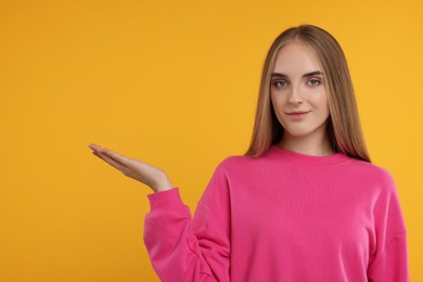 Special promotion. Young woman showing something on orange background, space for text