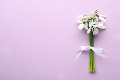 Beautiful bouquet of snowdrops on lilac background, top view. Space for text