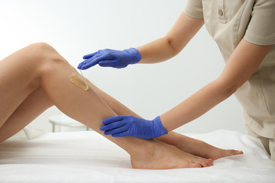 Photo of Woman getting wax epilation of legs in salon, closeup