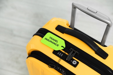 Photo of Above view of yellow suitcase with TRAVEL INSURANCE label indoors, closeup