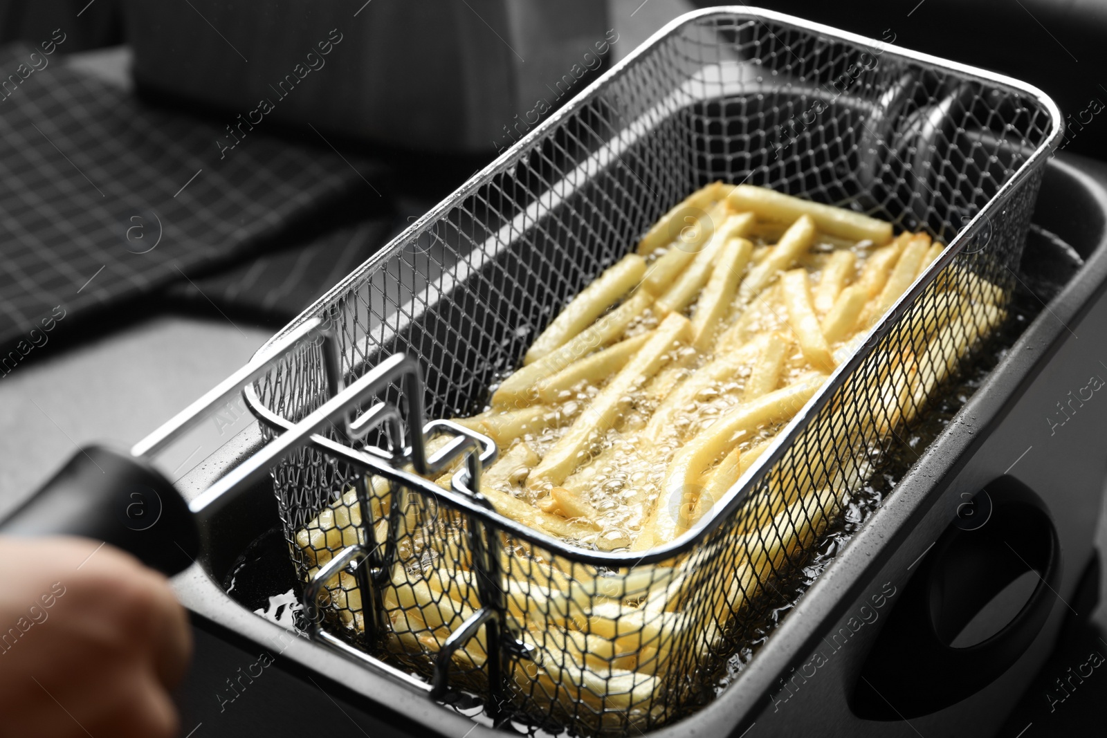 Photo of Cooking delicious french fries in hot oil, closeup