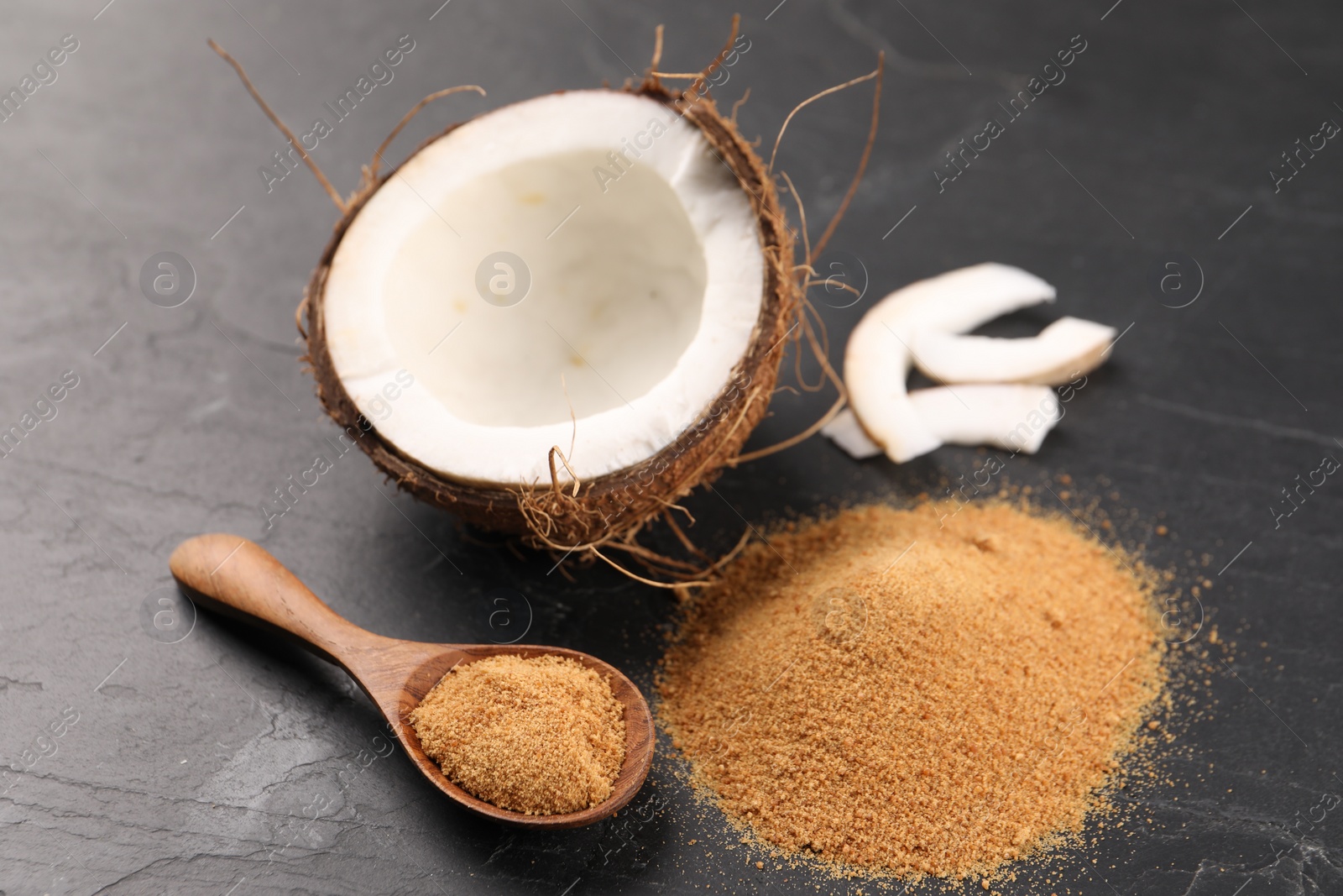 Photo of Coconut sugar, spoon and fruit on dark textured table, closeup