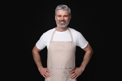 Happy man wearing kitchen apron on black background. Mockup for design