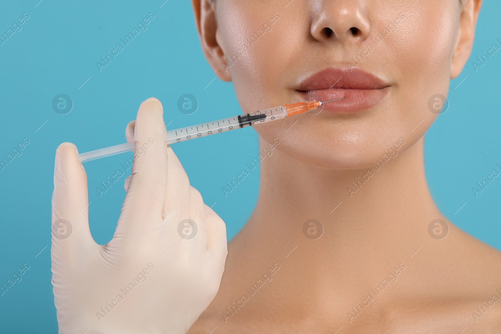 Photo of Doctor giving lips injection to young woman on light blue background, closeup. Cosmetic surgery