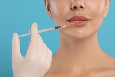 Doctor giving lips injection to young woman on light blue background, closeup. Cosmetic surgery