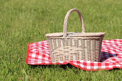 Photo of Picnic basket with checkered tablecloth on green grass outdoors, space for text