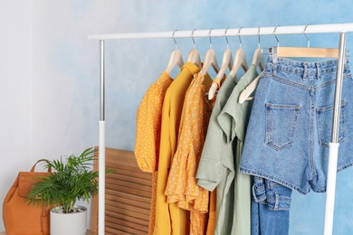 Photo of Rack with stylish clothes near light blue wall indoors