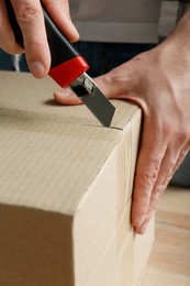 Photo of Man using utility knife to open parcel, closeup