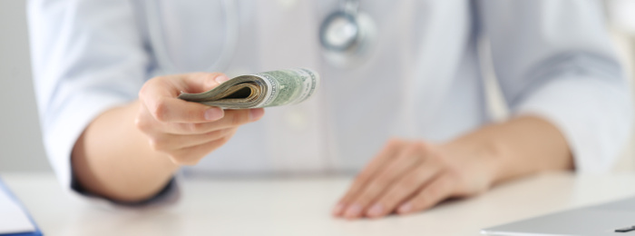 Doctor with bribe at desk in clinic, closeup. Banner design