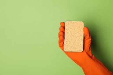 Woman in rubber glove holding sponge on green background, top view. Space for text