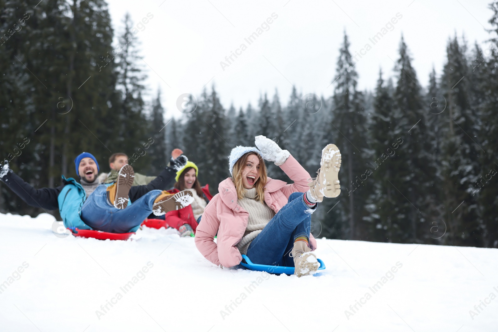 Photo of Happy friends sliding on sleds outdoors. Winter vacation