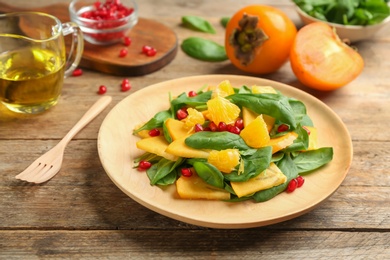 Photo of Delicious persimmon salad with pomegranate and spinach on wooden table