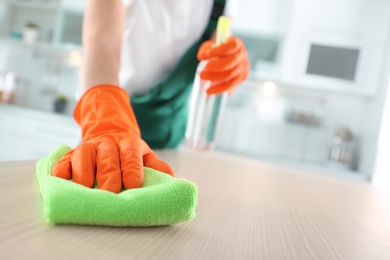 Worker in gloves cleaning table with rag, closeup. Space for text