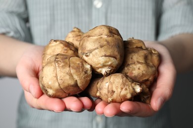 Photo of Woman holding Jerusalem artichokes on light grey background, closeup