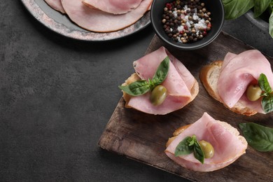 Photo of Delicious sandwiches with ham, basil, olives and spices on grey table, flat lay. Space for text