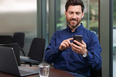 Photo of Handsome man using smartphone at table indoors