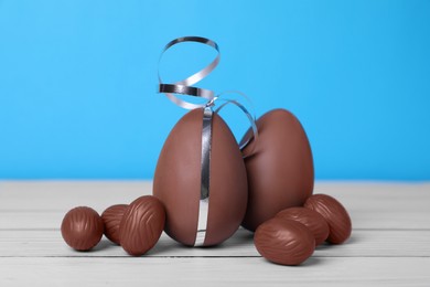 Delicious chocolate eggs and candies on white wooden table against light blue background, closeup