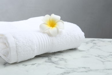 Photo of Folded terry towel and plumeria flower on white marble table, closeup. Space for text