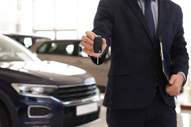 Photo of Salesman with key and clipboard in car salon, closeup