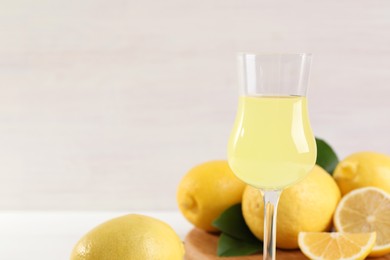 Liqueur glass with tasty limoncello, lemons and green leaves on table, closeup. Space for text