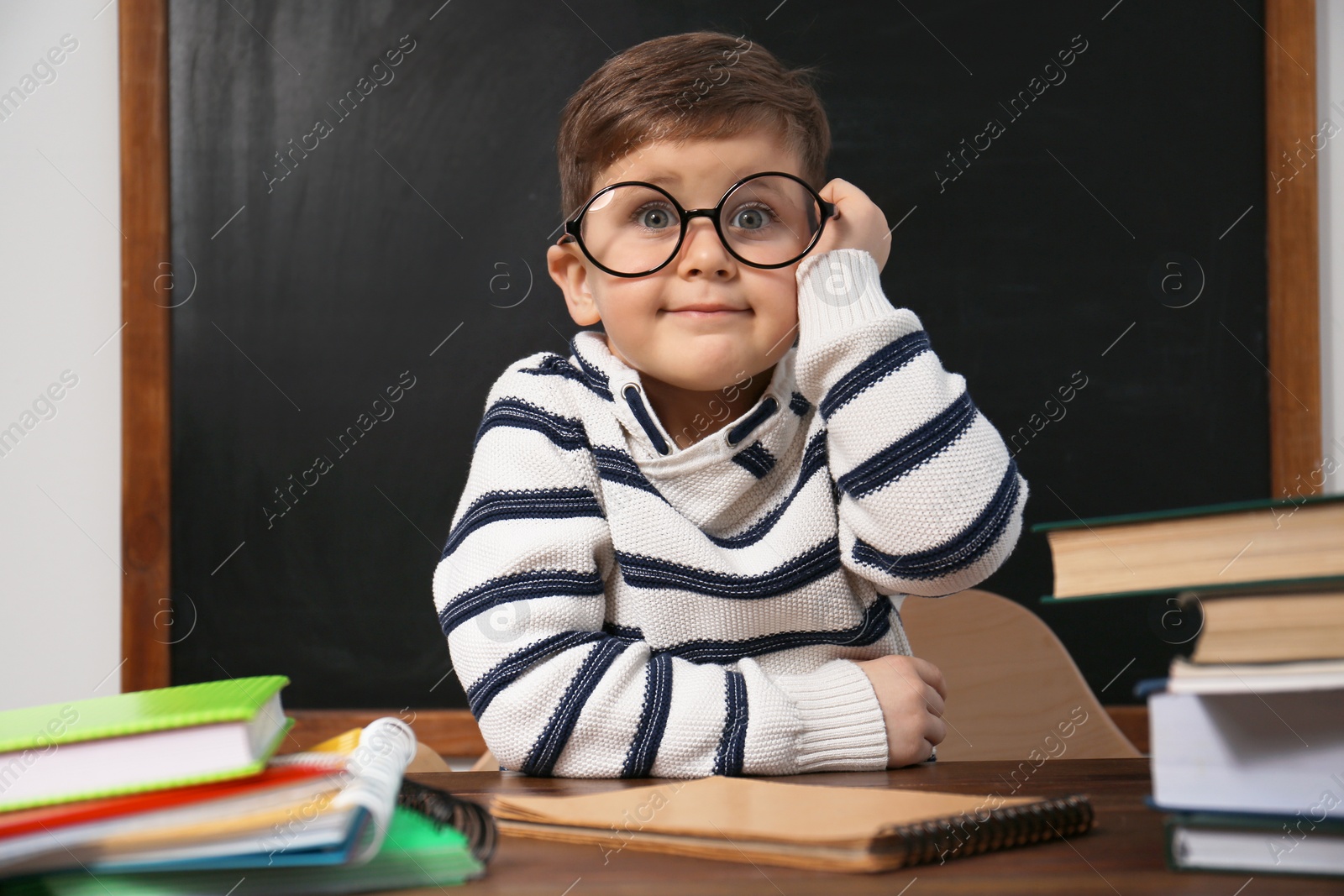 Photo of Cute little child wearing glasses at desk in classroom. First time at school