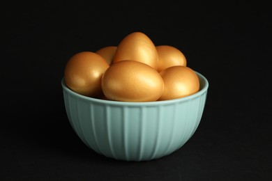 Photo of Shiny golden eggs in bowl on black background, closeup