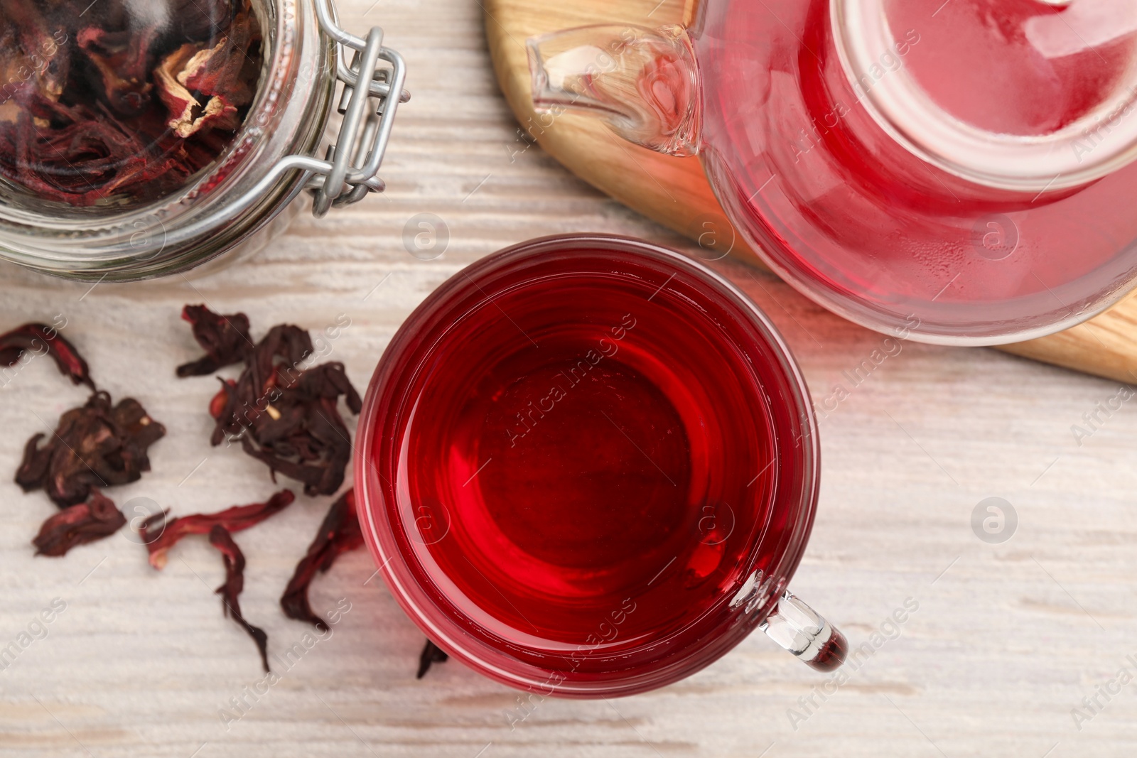 Photo of Delicious hibiscus tea and dry flowers on white wooden table, flat lay