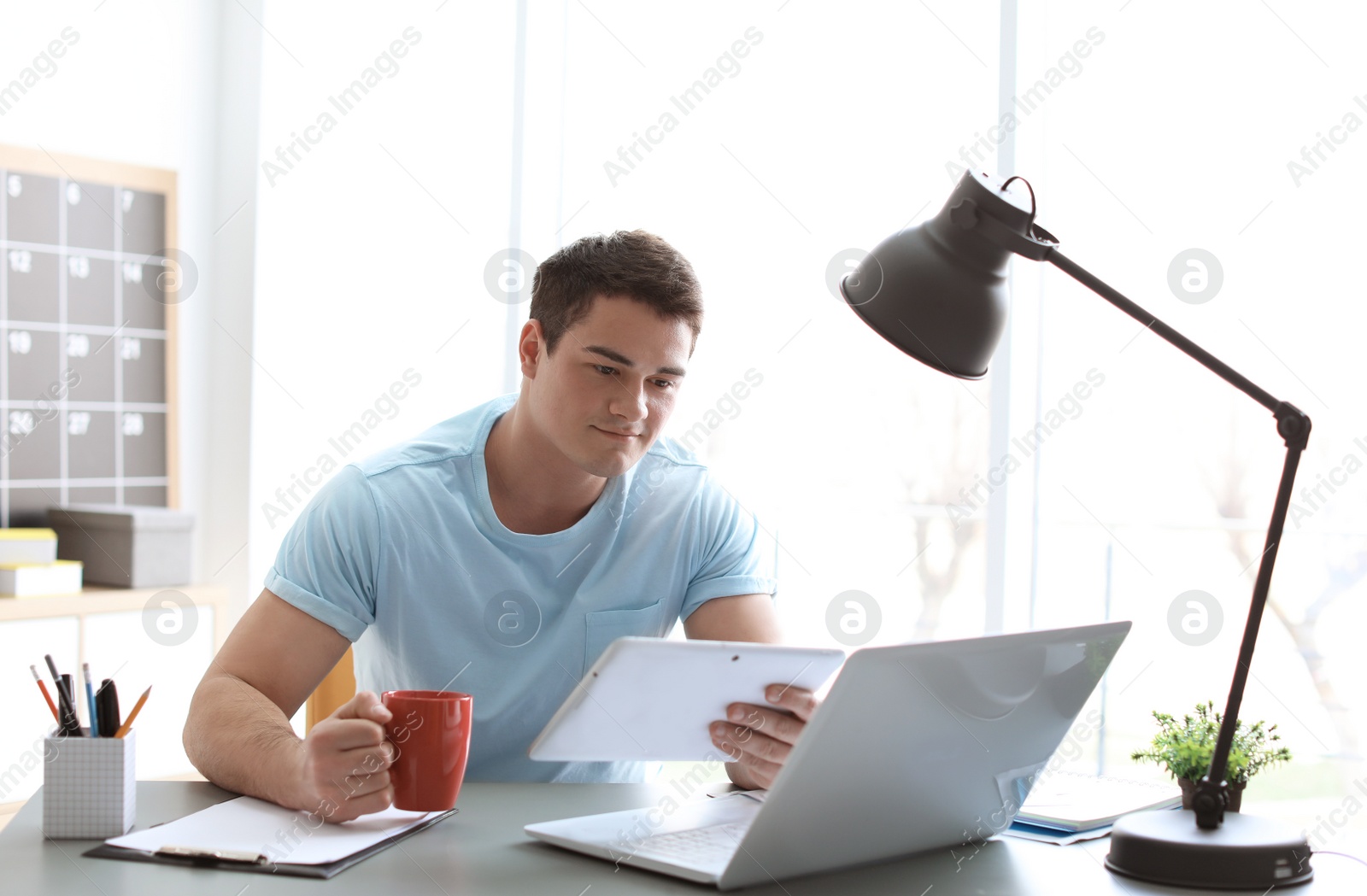 Photo of Portrait of confident young man with tablet and laptop and cup at table