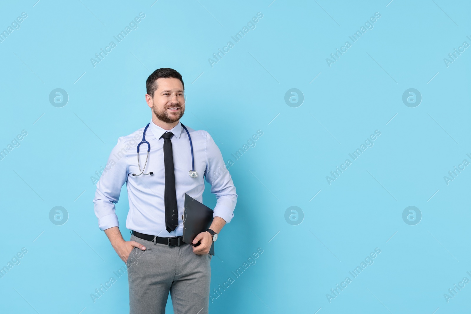 Photo of Smiling doctor with clipboard on light blue background. Space for text