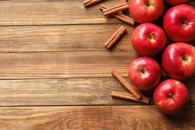 Photo of Fresh apples and cinnamon sticks on wooden table, top view