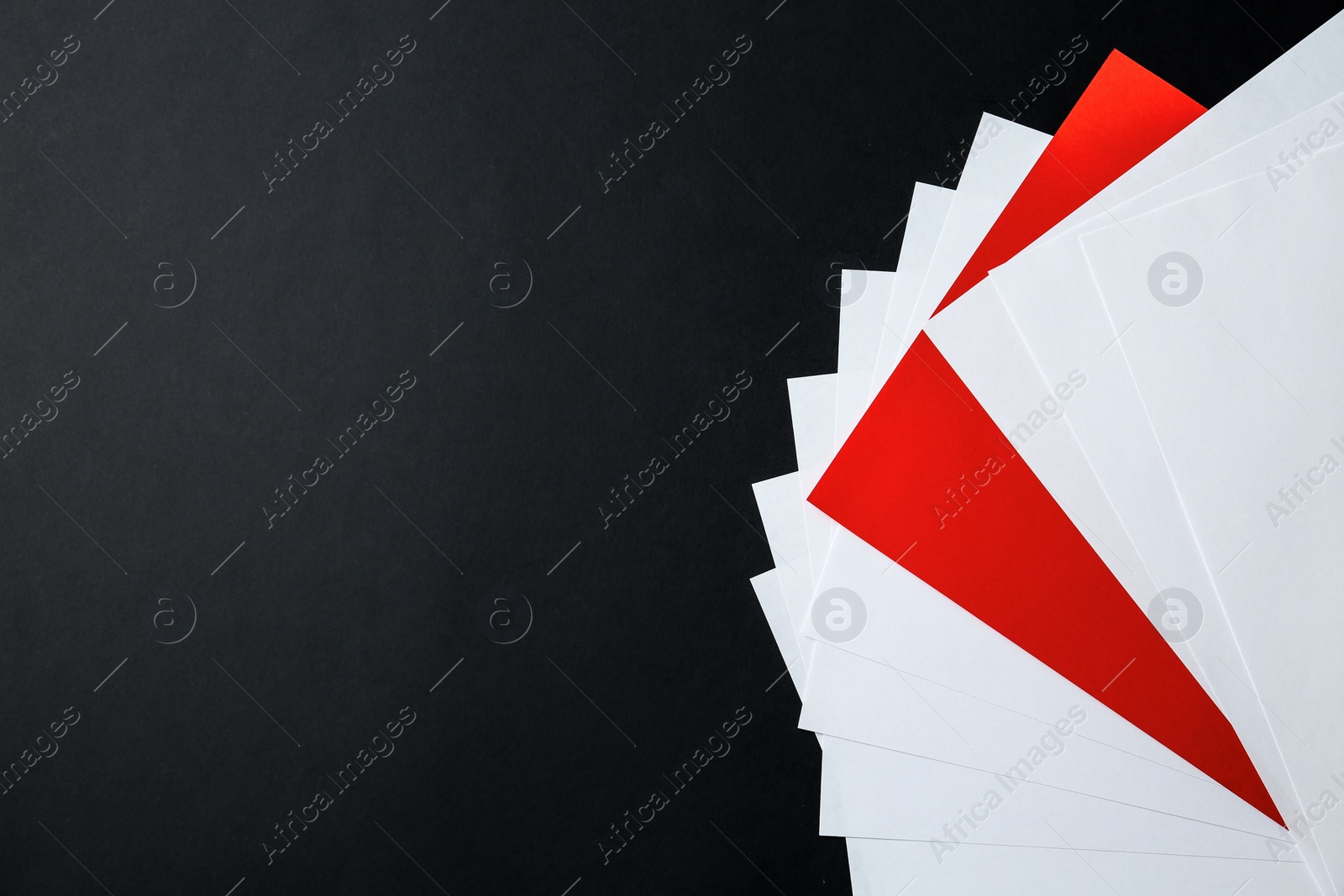 Photo of White paper sheets and different one on black background, flat lay. Space for text