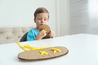 Little boy tying shoe lace using training cardboard template at white table indoors