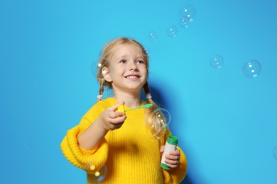 Photo of Cute little girl blowing soap bubbles on color background. Space for text