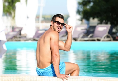 Photo of Handsome young man sitting at swimming pool edge on sunny day