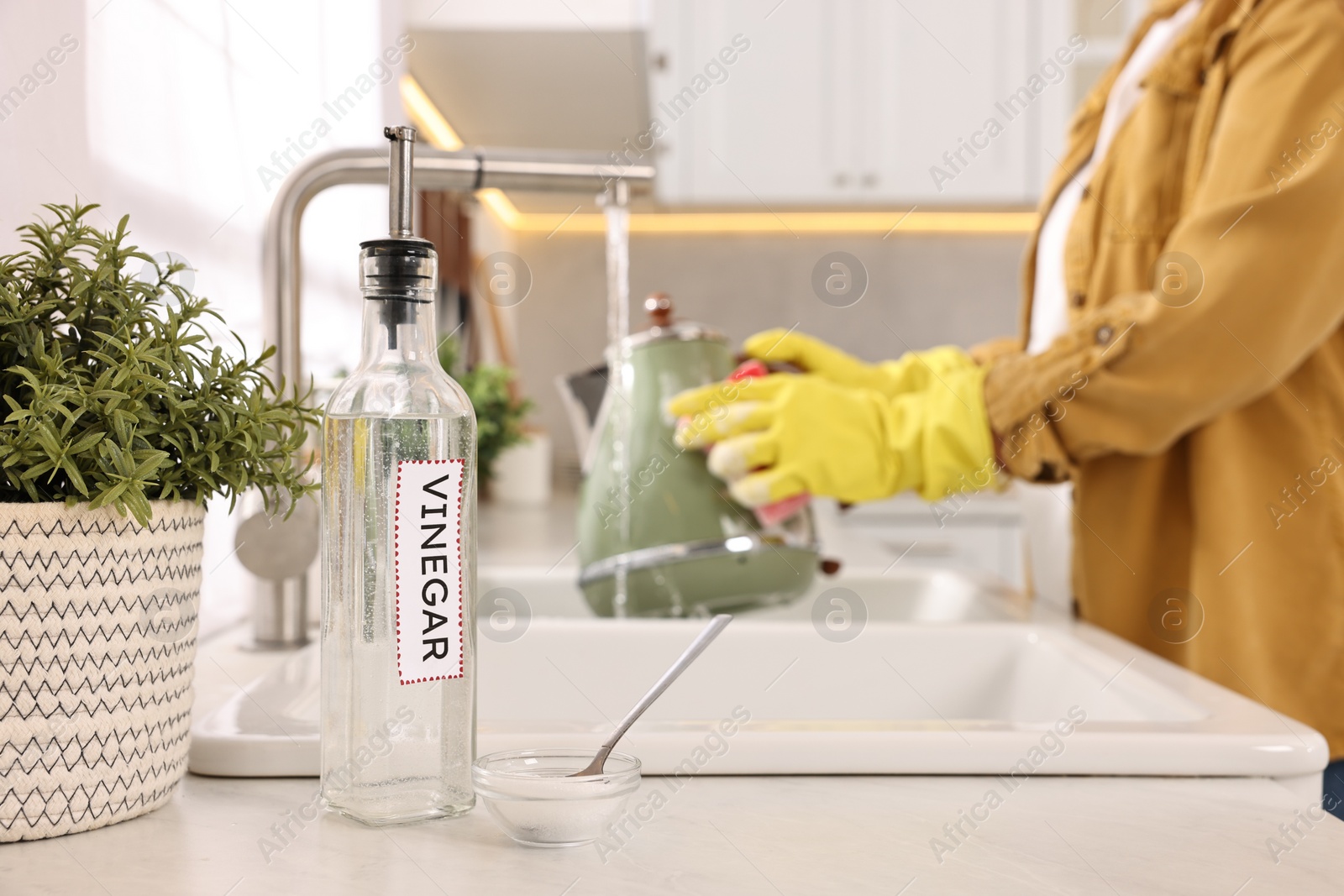 Photo of Woman washing electric kettle with sponge at sink in kitchen, focus on vinegar and baking soda