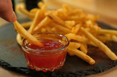 Photo of Woman eating tasty french fries with red sauce at table, closeup