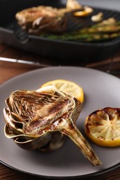 Tasty grilled artichoke and slices of lemon on table, closeup